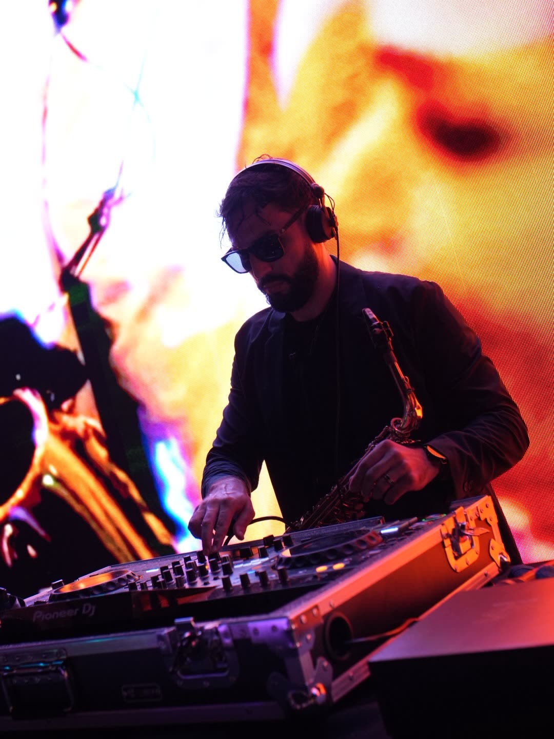 Bruno Daner em contraluz vermelha atrás do set de DJ com o saxofone