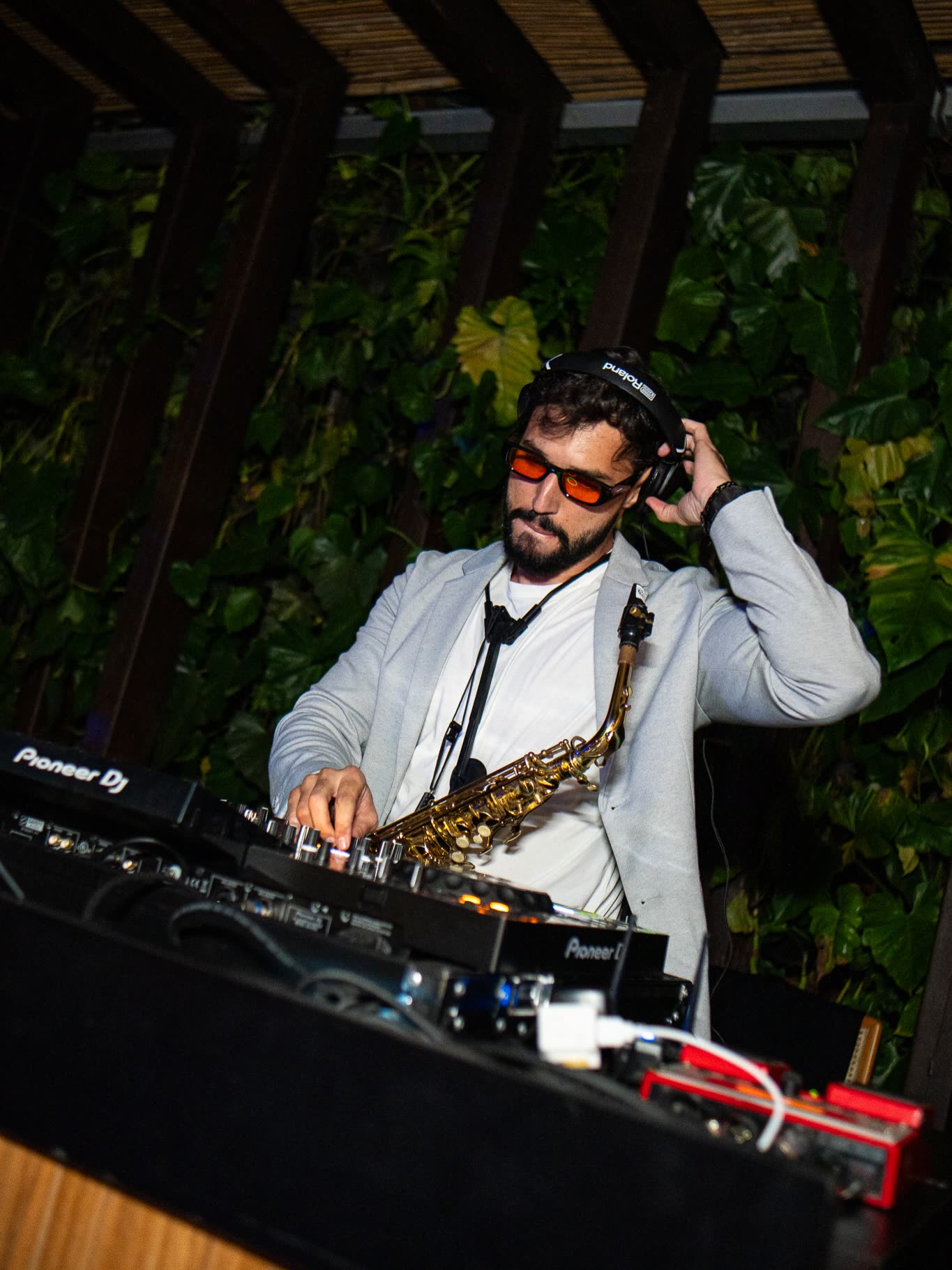 Bruno Daner de fones tocando saxofone sobre o mixer Pioneer DJ em festa ao ar livre