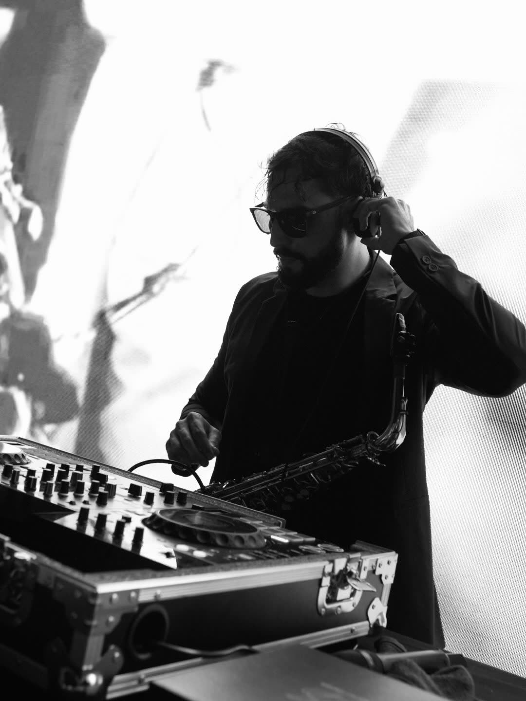 Bruno Daner em preto e branco tocando saxofone sobre o set de DJ